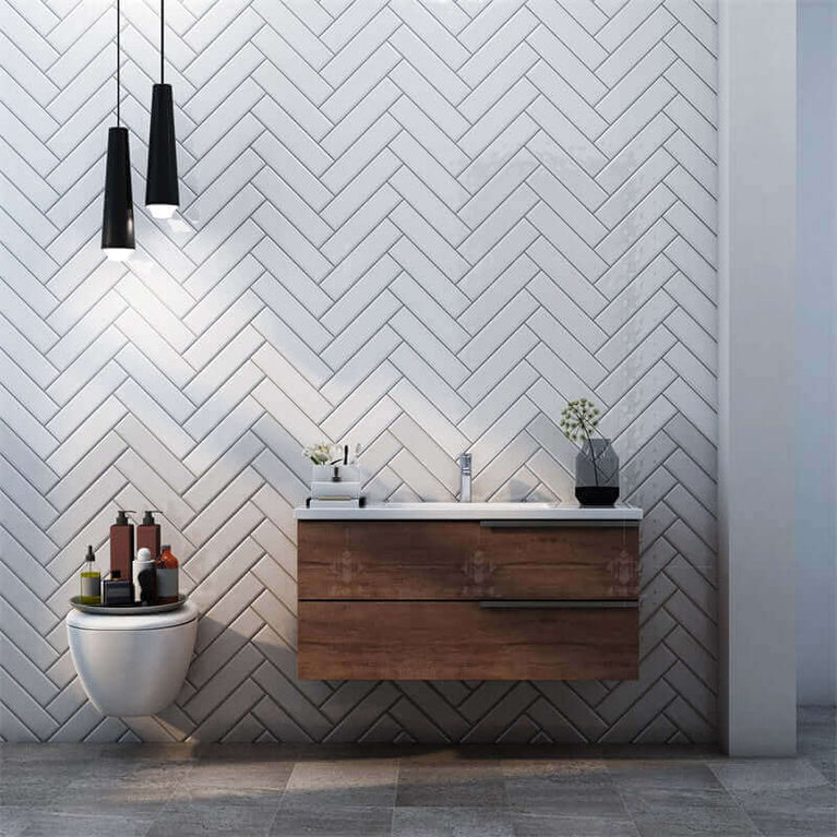 Salle de bain moderne avec carrelage blanc en chevron, meuble-vasque suspendu en bois, éclairage pendentif noir et accessoires décoratifs. Parfait pour mettre en valeur la céramique murale Métro blanche polie.