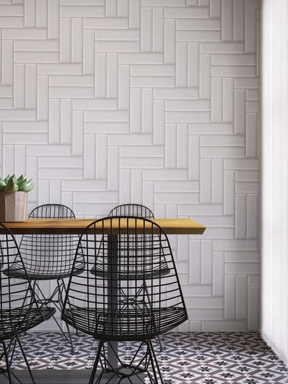 Carreaux de métro blancs en céramique disposés en motif chevron sur un mur de cuisine moderne, avec table en bois et chaises en métal noir, créant un contraste élégant et un design contemporain