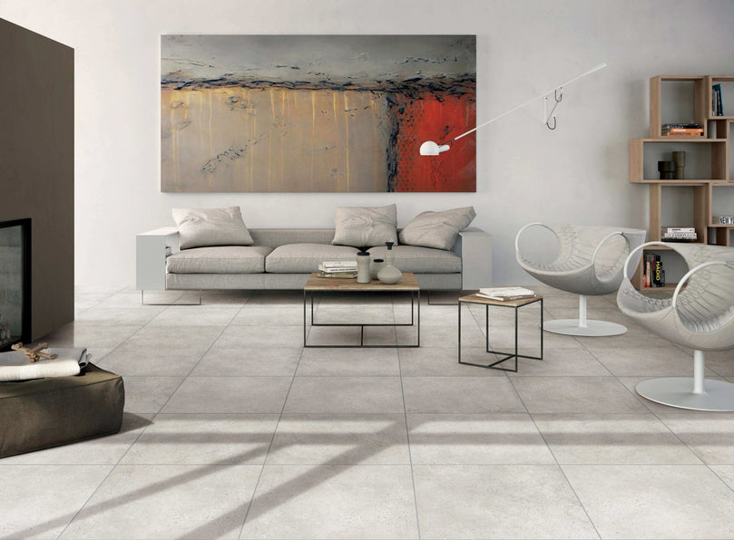 Salon moderne avec carrelage Céramique Stone Cement Grège au sol, canapé gris, tableau abstrait et mobilier contemporain, illustrant l'élégance et la polyvalence du carrelage pour sols et murs dans un espace résidentiel
