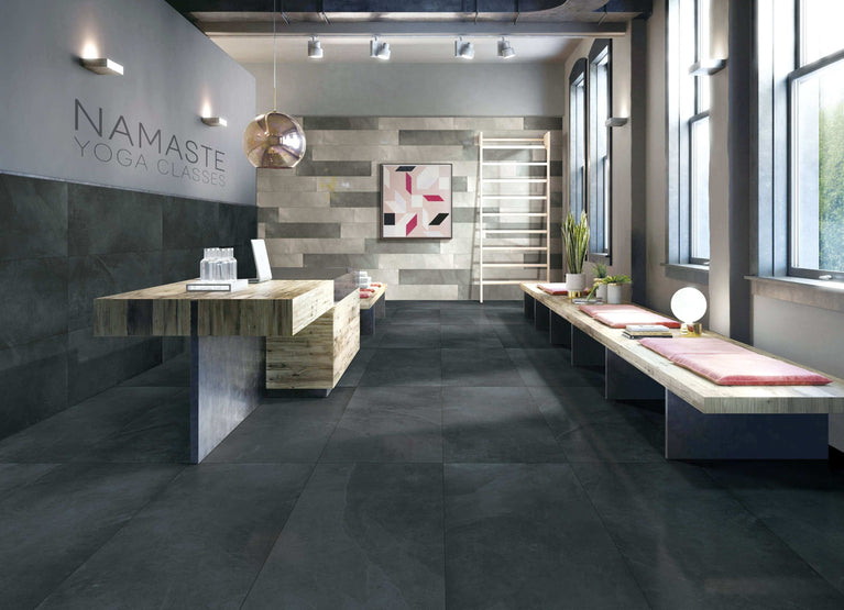 Intérieur moderne d'un studio de yoga avec sol en céramique noire Mustang. Espace lumineux et épuré avec murs gris, éléments en bois naturel et décoration minimaliste. Parfait pour illustrer l'utilisation du carrelage Céramique Mustang Black dans un cadre commercial élégant.