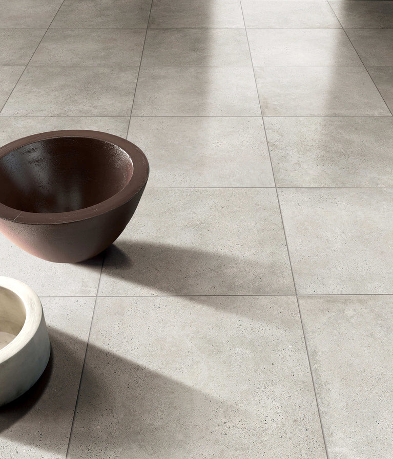 Carrelage Céramique Stone Cement Grège 24x24 pouces, surface mate pour sol et mur, avec deux bols décoratifs sur le plancher, illustrant la texture et la couleur du produit dans un espace intérieur élégant et minimaliste.