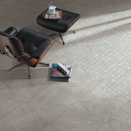 Carrelage Céramique Marble Stone Grigio 24"x48" dans un salon moderne avec fauteuil en cuir noir, table basse et livres, illustrant l'élégance et la polyvalence du produit pour sols et murs résidentiels ou commerciaux