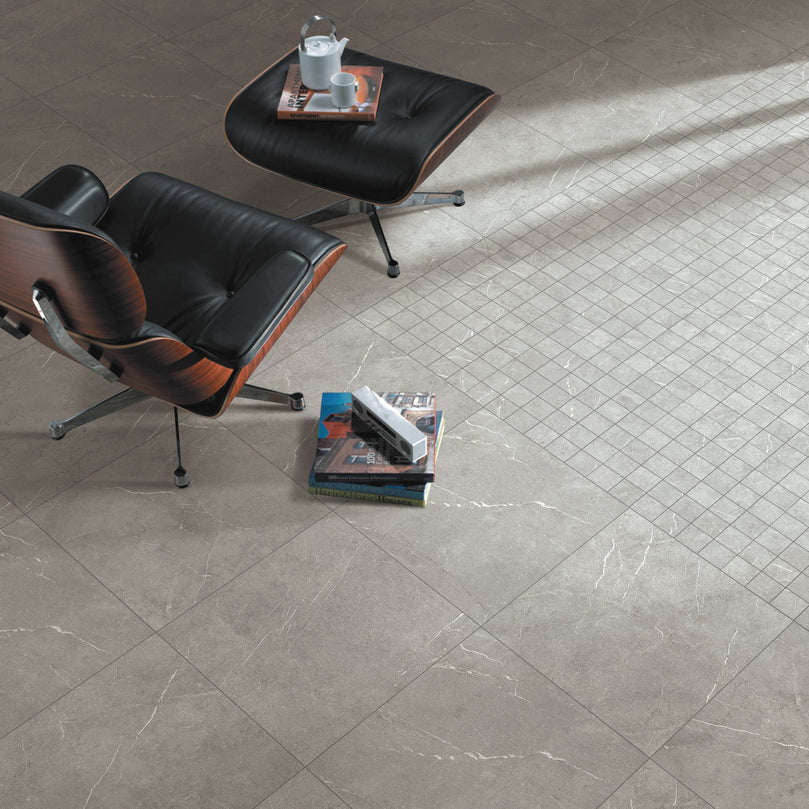Carrelage Céramique Marble Stone Grigio 24"x48" dans un salon moderne avec fauteuil en cuir noir, table basse et livres, illustrant l'élégance et la polyvalence du produit pour sols et murs résidentiels ou commerciaux