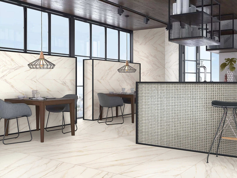 Intérieur élégant avec carrelage Céramique Marble Stone Oro 24"x48" au sol et murs, cuisine ouverte avec îlot, espace repas avec tables en bois et chaises grises, luminaires suspendus géométriques, grandes fenêtres offrant beaucoup de lumière naturelle