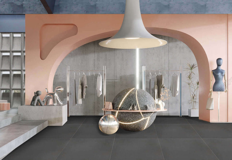 Intérieur moderne avec carrelage Céramique Plain Carbon au sol, murs roses et gris, grande arche, luminaire suspendu et décorations sphériques. Espace boutique élégant et minimaliste.